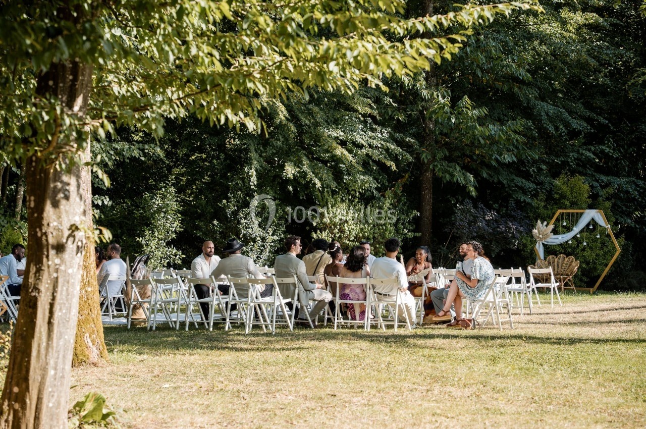 Cérémonie en plein air avec des invités assis sur des chaises blanches, entourés de verdure et d'un décor minimaliste.