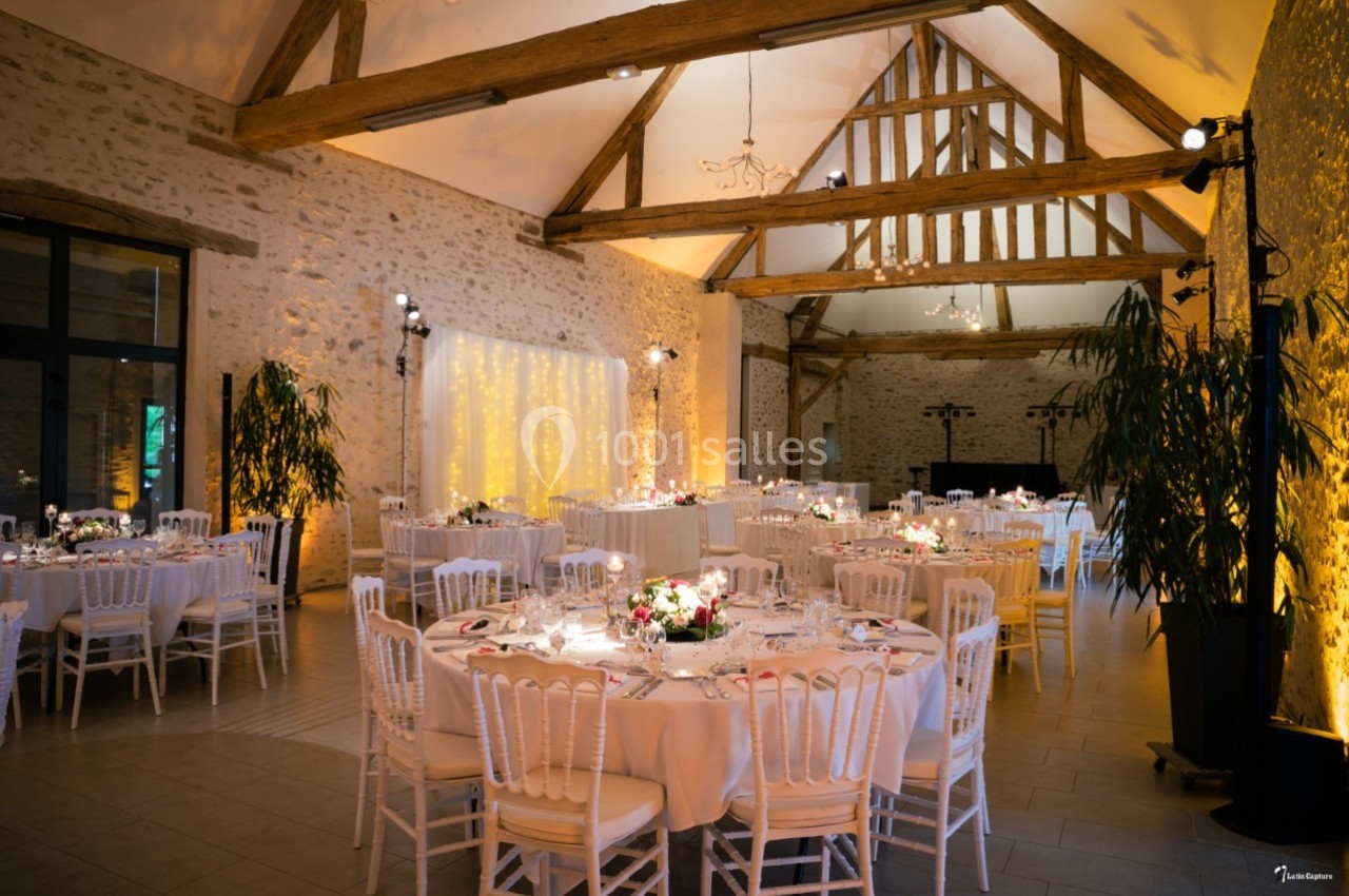 Salle de réception avec murs en pierre, poutres apparentes, tables décorées et éclairage chaleureux.
