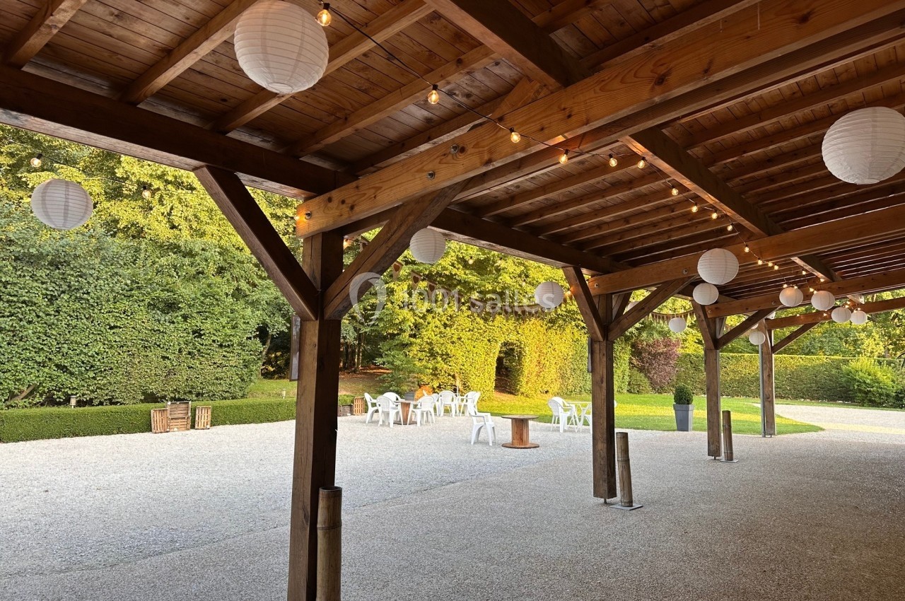 Structure en bois avec lanternes suspendues, donnant sur une cour gravillonnée et un jardin verdoyant en arrière-plan.
