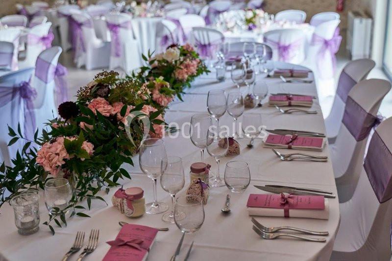Tables de réception décorées avec des fleurs, nappes blanches, rubans violets et menus roses.