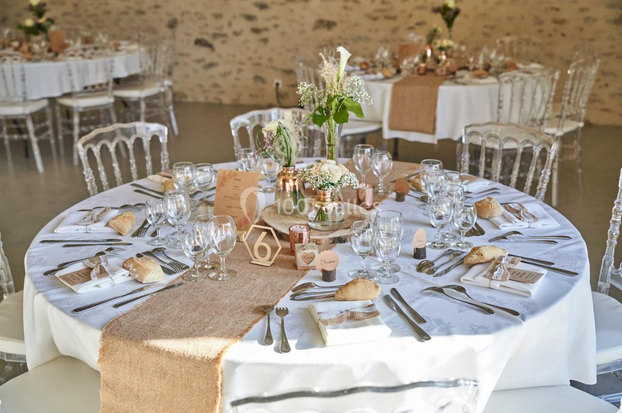Table de réception décorée avec nappes blanches, chemins de table en jute, vaisselle élégante et centre de table floral.