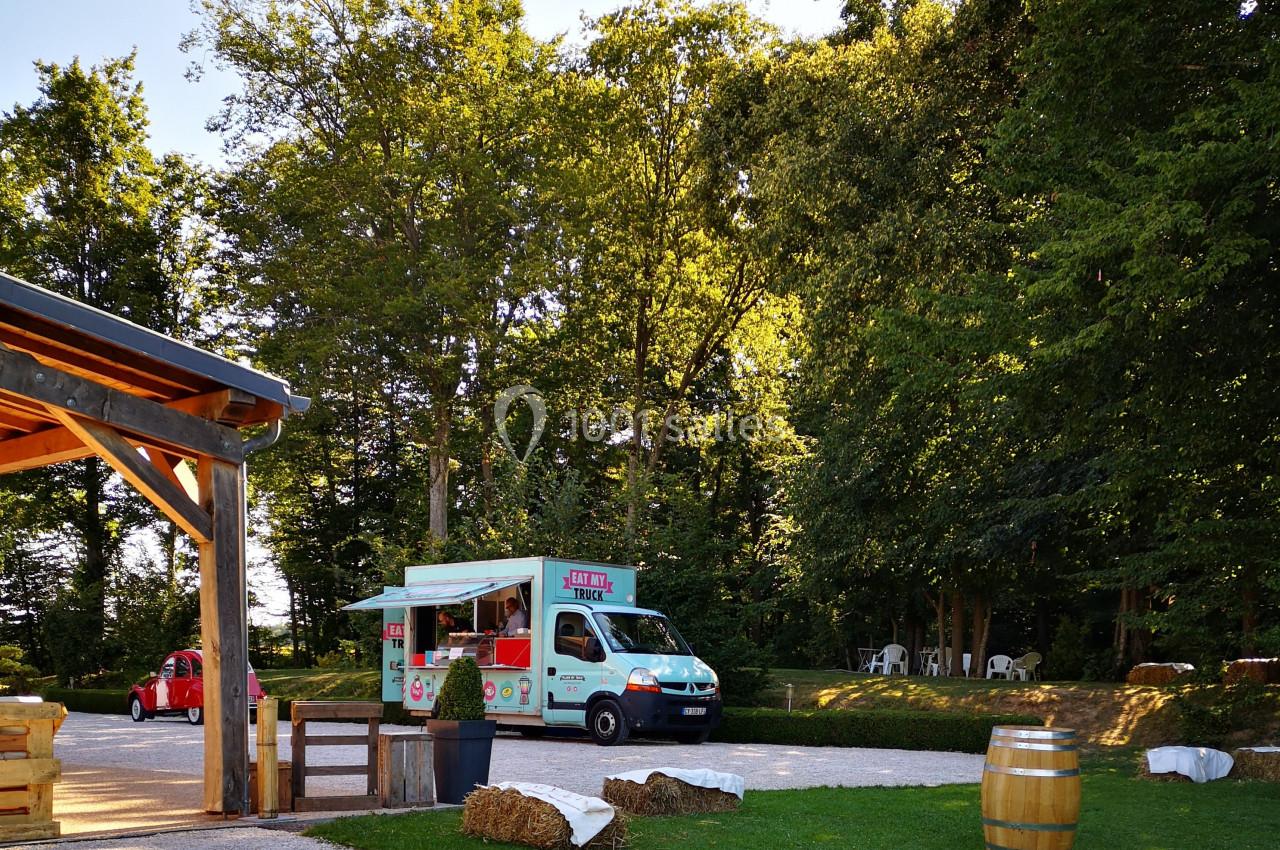 Camion de restauration coloré stationné dans un espace verdoyant près d'une terrasse en bois et de tables extérieures.