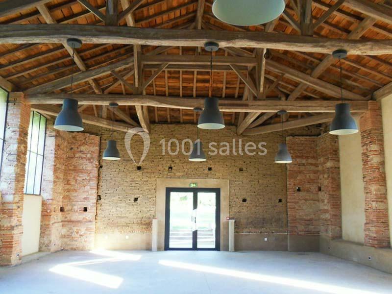 Salle intérieure avec murs en briques apparentes, poutres en bois au plafond et grandes suspensions lumineuses.