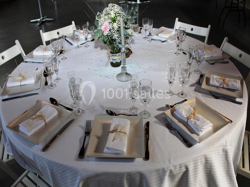 Table ronde dressée avec une nappe blanche, vaisselle élégante, serviettes pliées et un centre de table floral.