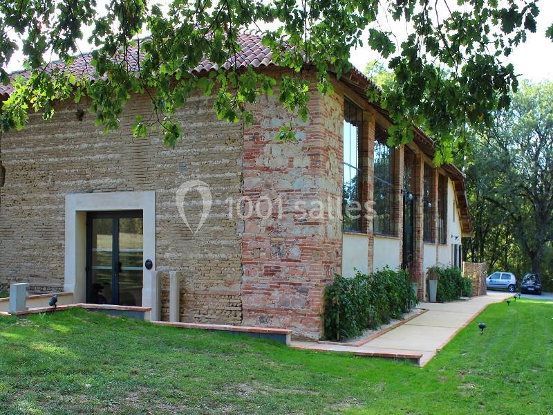 Bâtiment en briques et pierre avec de grandes fenêtres, entouré de verdure et partiellement ombragé par des arbres.