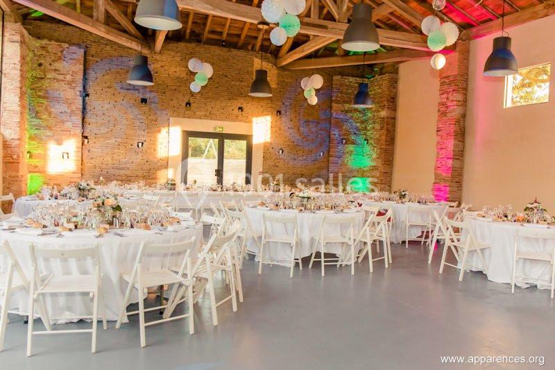 Salle de réception décorée avec des tables rondes dressées, des chaises blanches et des éclairages colorés sur les murs en…