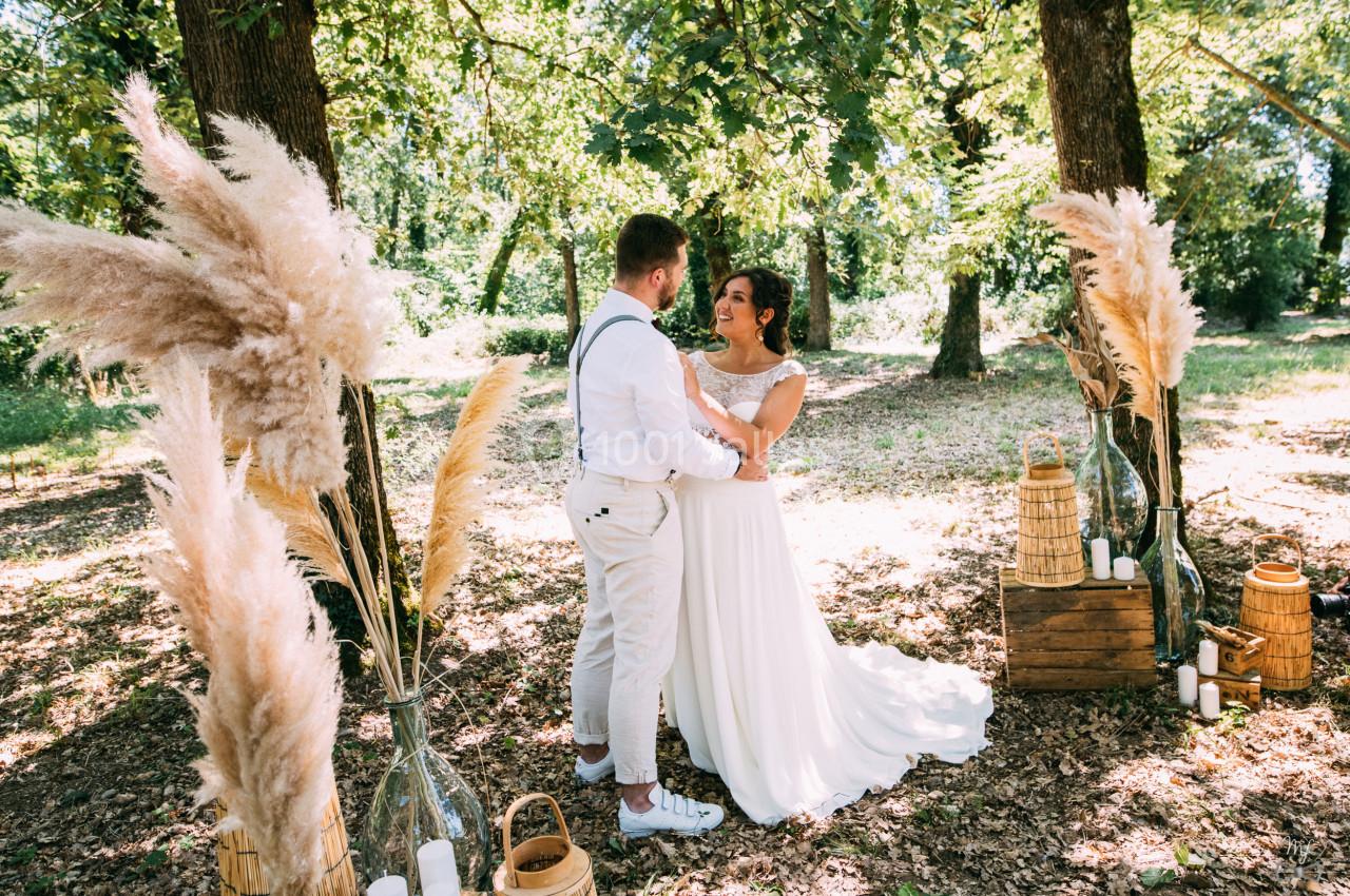 Un couple en tenue de mariage se tient sous des arbres, entouré de décorations naturelles et de pampas.