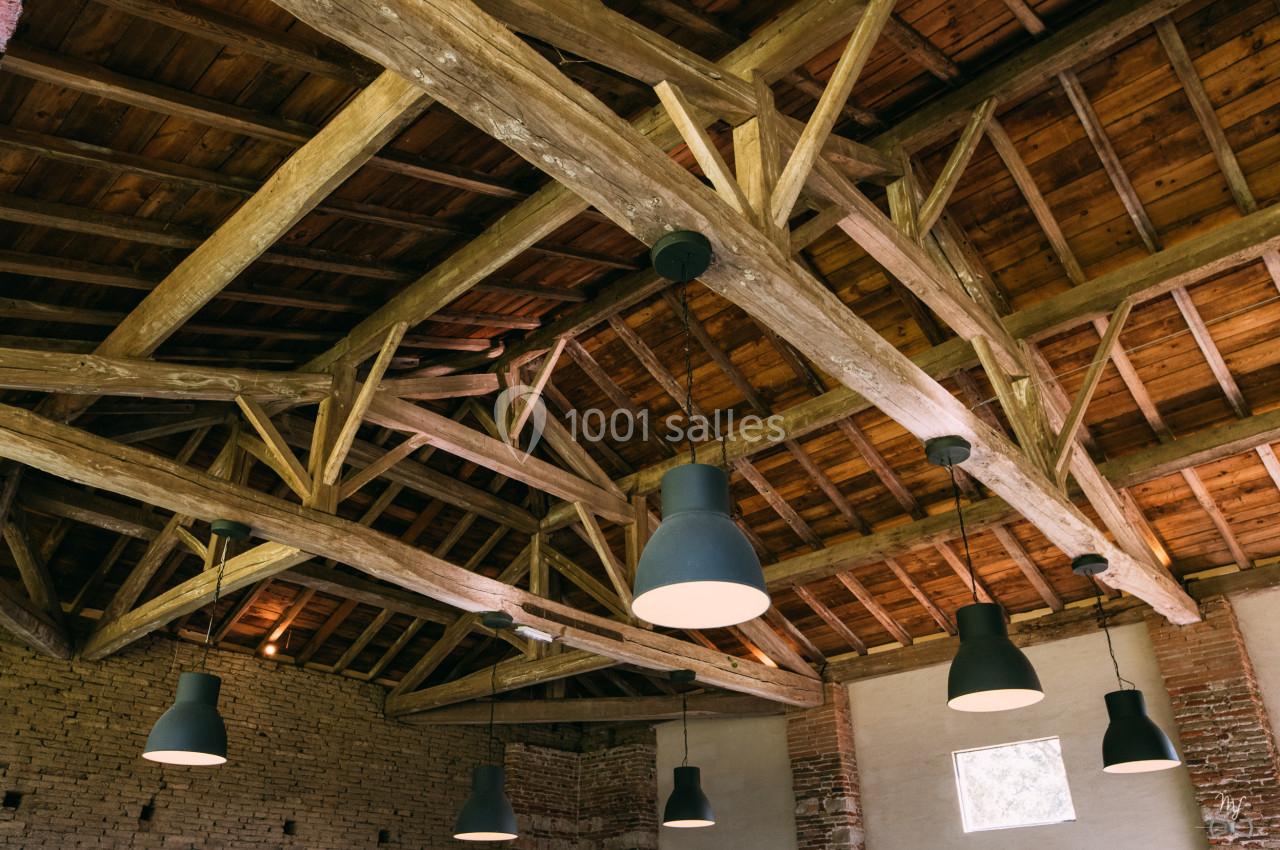 Plafond en bois avec poutres apparentes et plusieurs suspensions lumineuses dans une pièce en briques.
