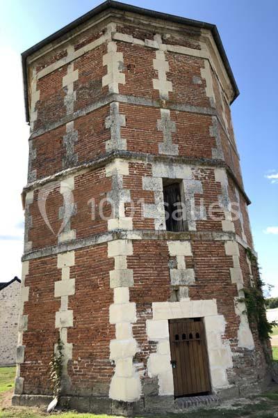 Tour octogonale en briques rouges et pierres blanches avec une porte en bois, située dans un environnement rural.