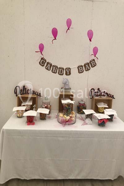 Table de candy bar décorée avec des bonbonnières remplies de sucreries, ballons roses et pancartes ’Delicious’.