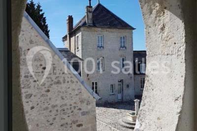 Canapé gris avec coussins, table basse avec magazines et télécommande, tableau mural et fenêtre laissant entrer la lumière.