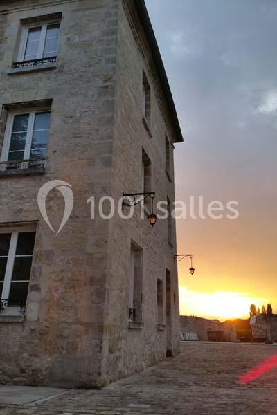 Façade en pierre d'un bâtiment ancien éclairé par un coucher de soleil, avec des lampes murales allumées.