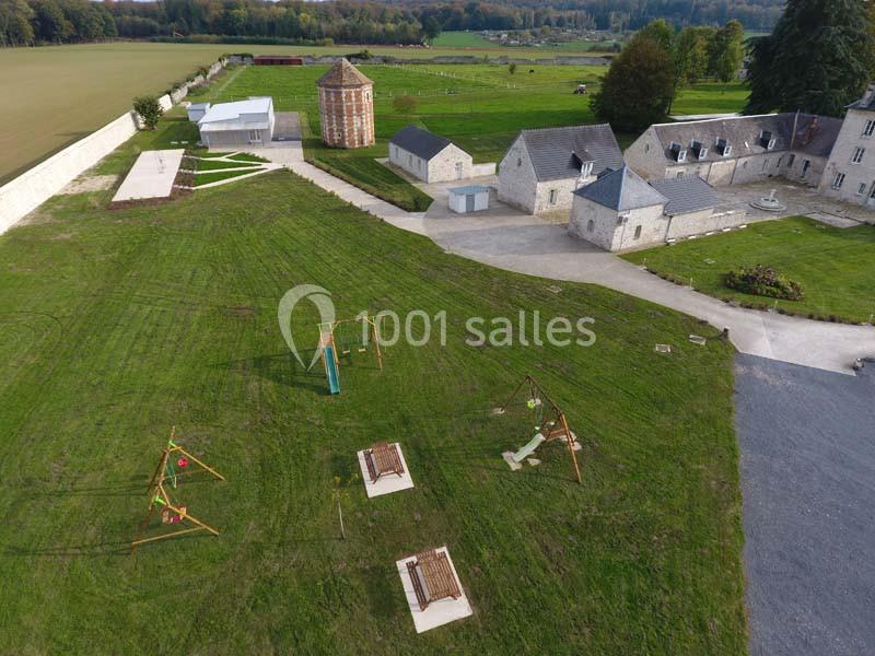 Vue aérienne d'une aire de jeux sur pelouse avec bâtiments en pierre et tour cylindrique en arrière-plan.