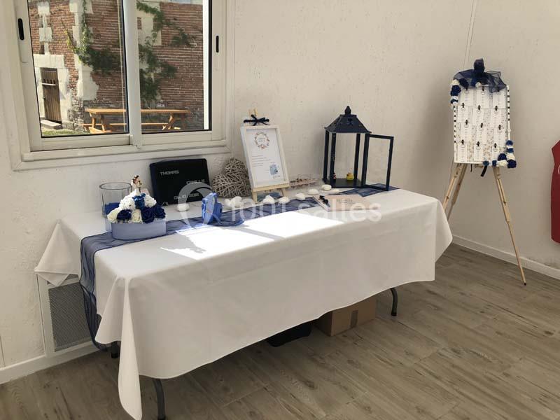 Table décorée avec des éléments marins, lanternes et fleurs, placée près d'une fenêtre dans une salle lumineuse.