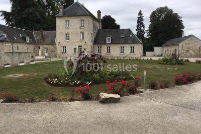 Canapé gris avec coussins, table basse avec magazines et télécommande, tableau mural et fenêtre laissant entrer la lumière.