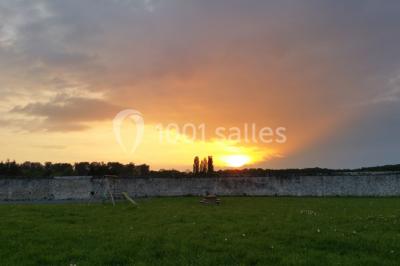 Canapé gris avec coussins, table basse avec magazines et télécommande, tableau mural et fenêtre laissant entrer la lumière.