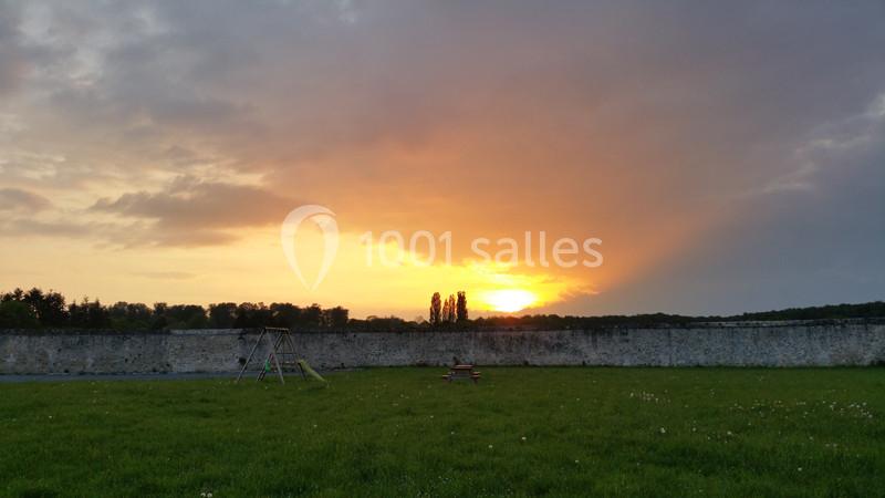 Coucher de soleil derrière un mur de pierre, avec une aire de jeux et une prairie au premier plan.