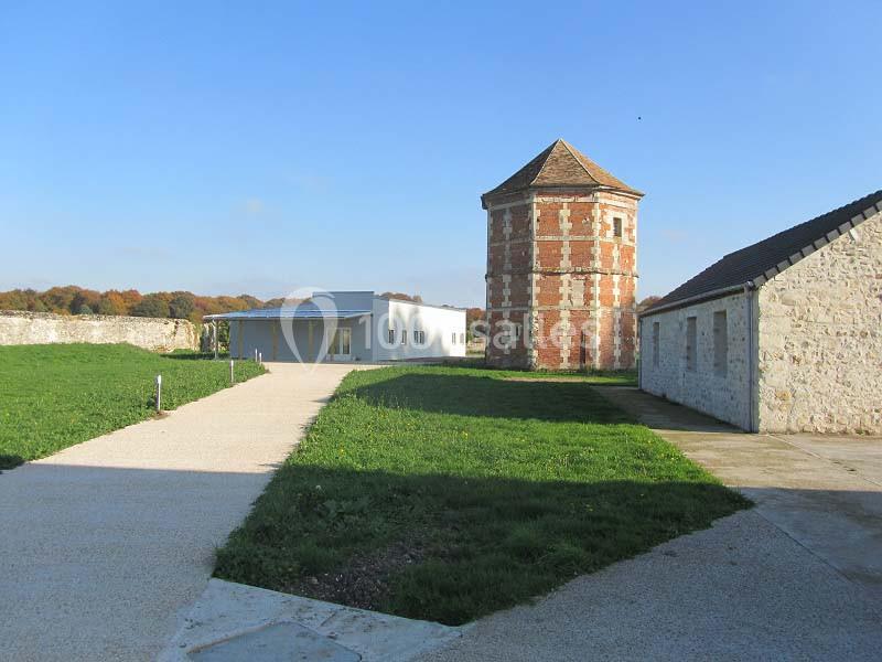 Allée pavée menant à un bâtiment moderne, une tour en briques et des bâtiments en pierre dans un espace verdoyant.
