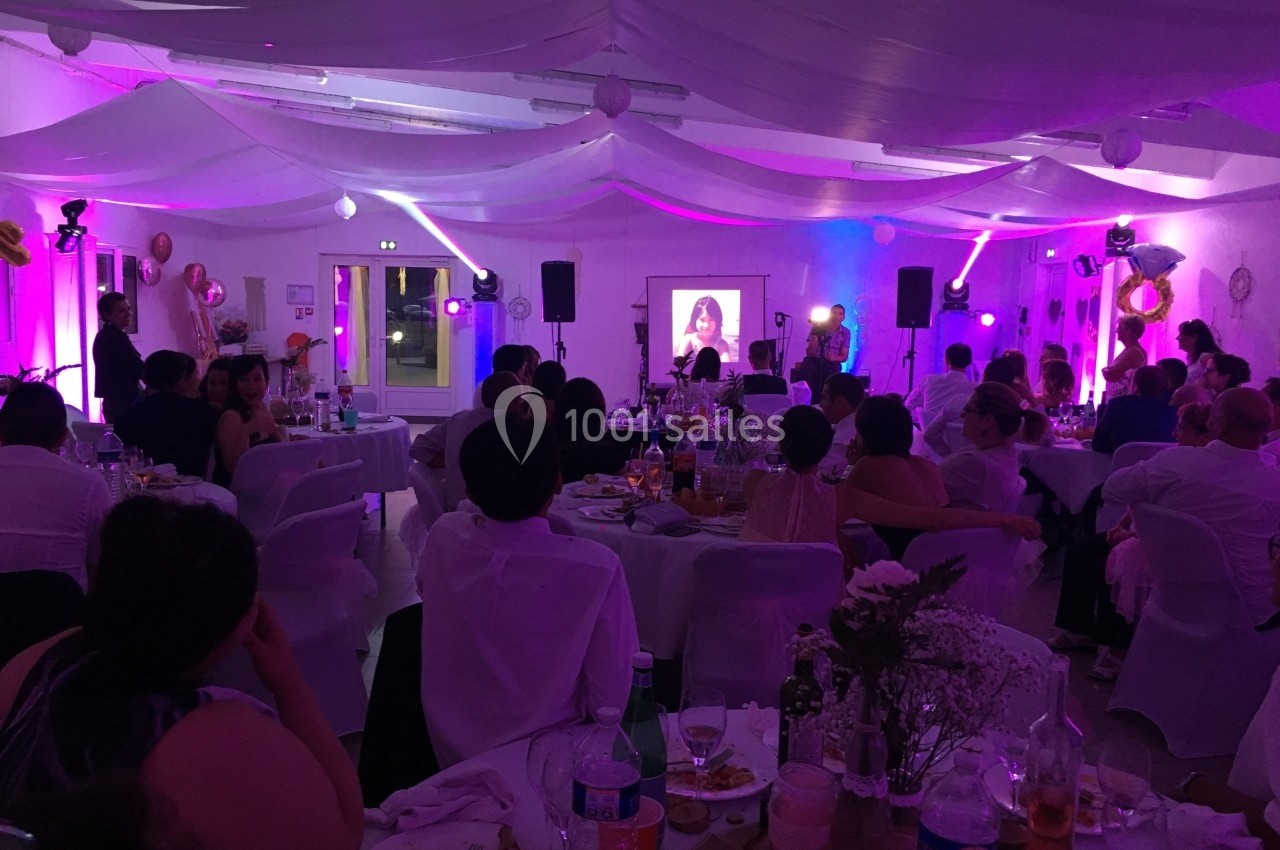 Salle de réception décorée avec des invités assis, éclairage coloré et projection d'une image sur un écran.