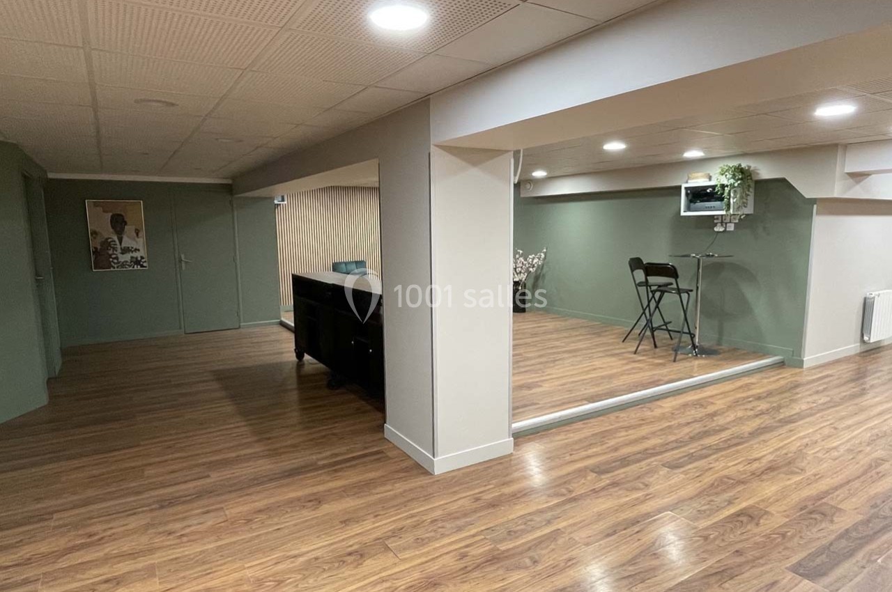 Sous-sol aménagé avec parquet, murs verts et beige, espace salon et coin repas avec table et chaises pliantes.