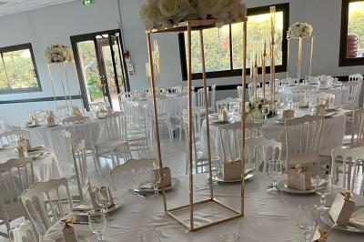 Salle de réception décorée avec des tables rondes dressées, nappes blanches, chaises blanches et touches de rose.