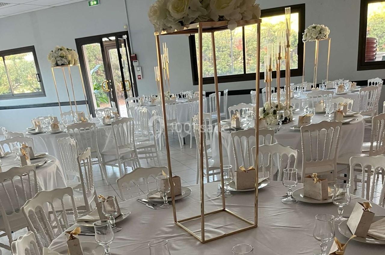 Salle de réception décorée avec des tables rondes, nappes blanches, chaises assorties et centres de table floraux.