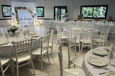 Salle de réception décorée avec des tables rondes dressées, nappes blanches, chaises blanches et touches de rose.