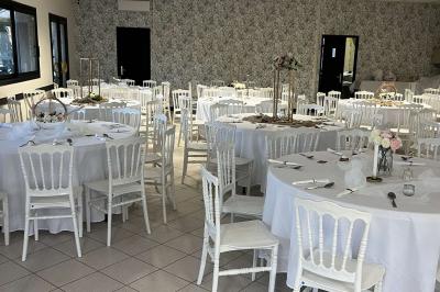Salle de réception décorée avec des tables rondes dressées, nappes blanches, chaises blanches et touches de rose.