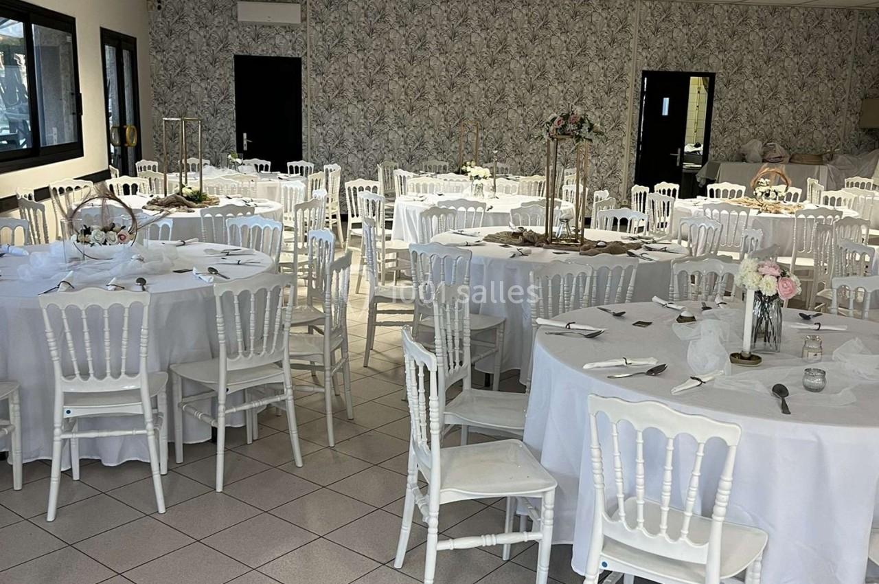 Salle de réception décorée avec des tables rondes, nappes blanches, chaises blanches et centres de table floraux.