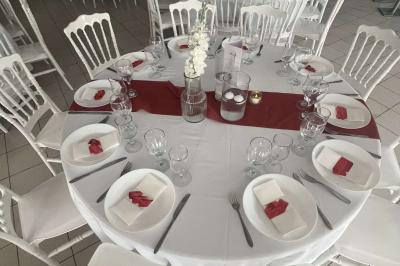 Salle de réception décorée avec des tables rondes dressées, nappes blanches, chaises blanches et touches de rose.