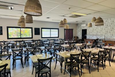 Salle de réception décorée avec des tables rondes dressées, nappes blanches, chaises blanches et touches de rose.
