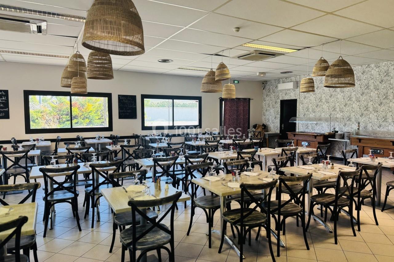 Salle de restaurant lumineuse avec tables dressées, chaises en bois et suspensions en osier au plafond.