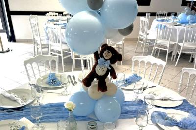 Salle de réception décorée avec des tables rondes dressées, nappes blanches, chaises blanches et touches de rose.