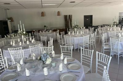 Salle de réception décorée avec des tables rondes dressées, nappes blanches, chaises blanches et touches de rose.