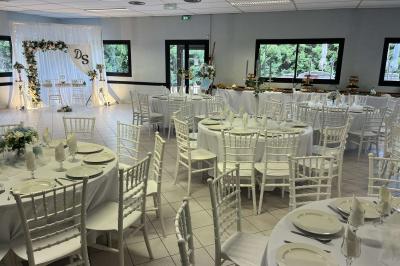 Salle de réception décorée avec des tables rondes dressées, nappes blanches, chaises blanches et touches de rose.