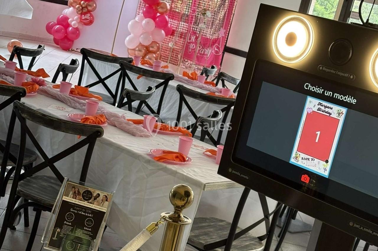 Salle décorée pour un événement avec une table dressée et une borne photo interactive au premier plan.