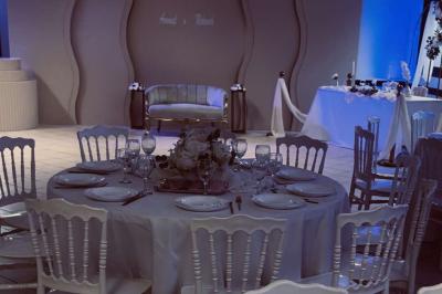 Salle de réception décorée avec des tables rondes dressées, nappes blanches, chaises blanches et touches de rose.
