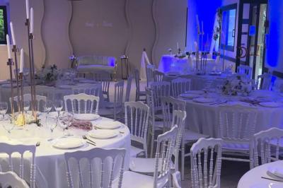 Salle de réception décorée avec des tables rondes dressées, nappes blanches, chaises blanches et touches de rose.