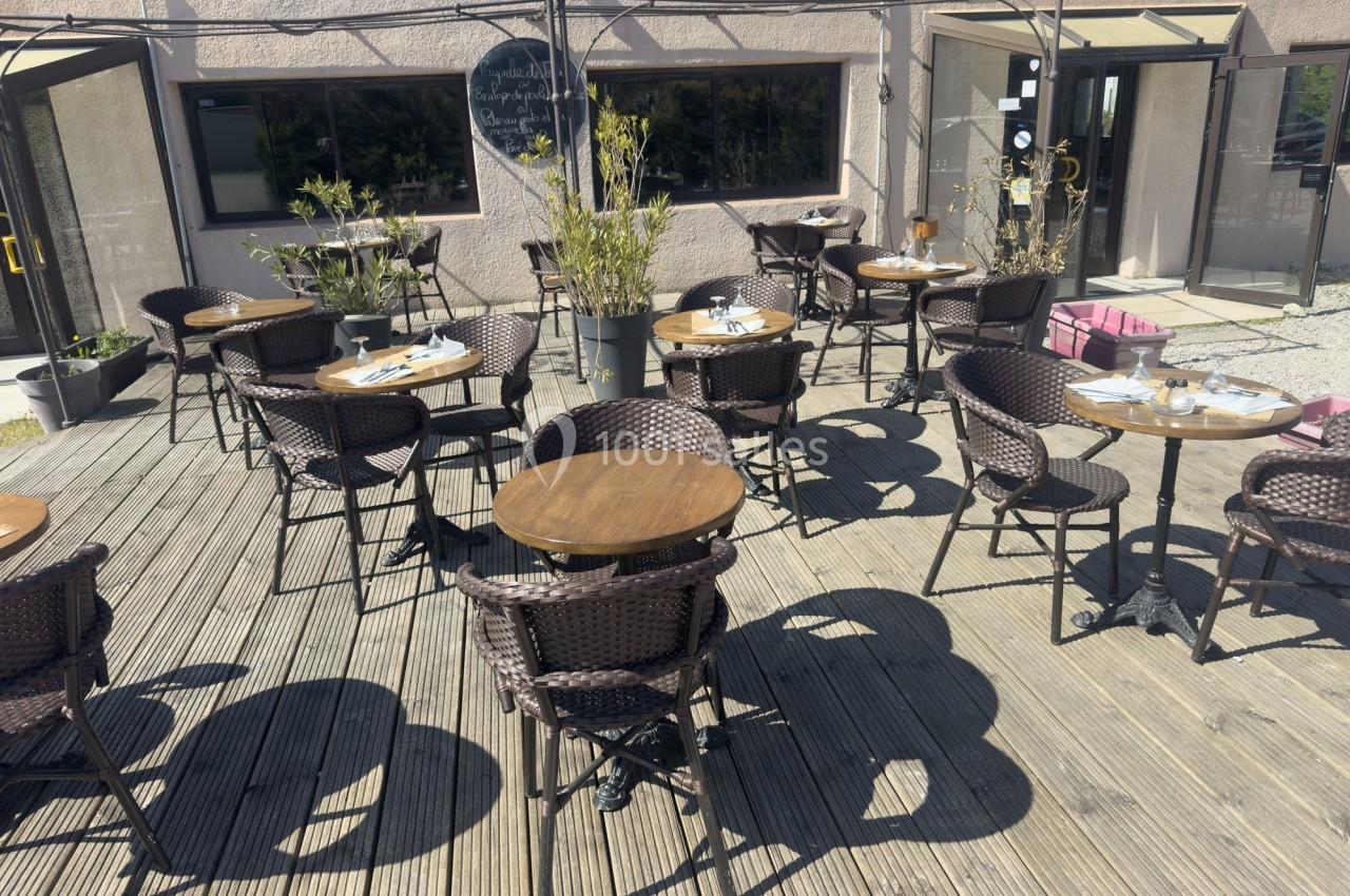 Terrasse en bois avec des tables rondes et des chaises en rotin, entourée de plantes et baignée de lumière naturelle.