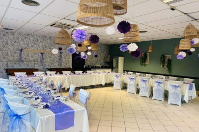Salle de réception décorée avec des tables rondes dressées, nappes blanches, chaises blanches et touches de rose.