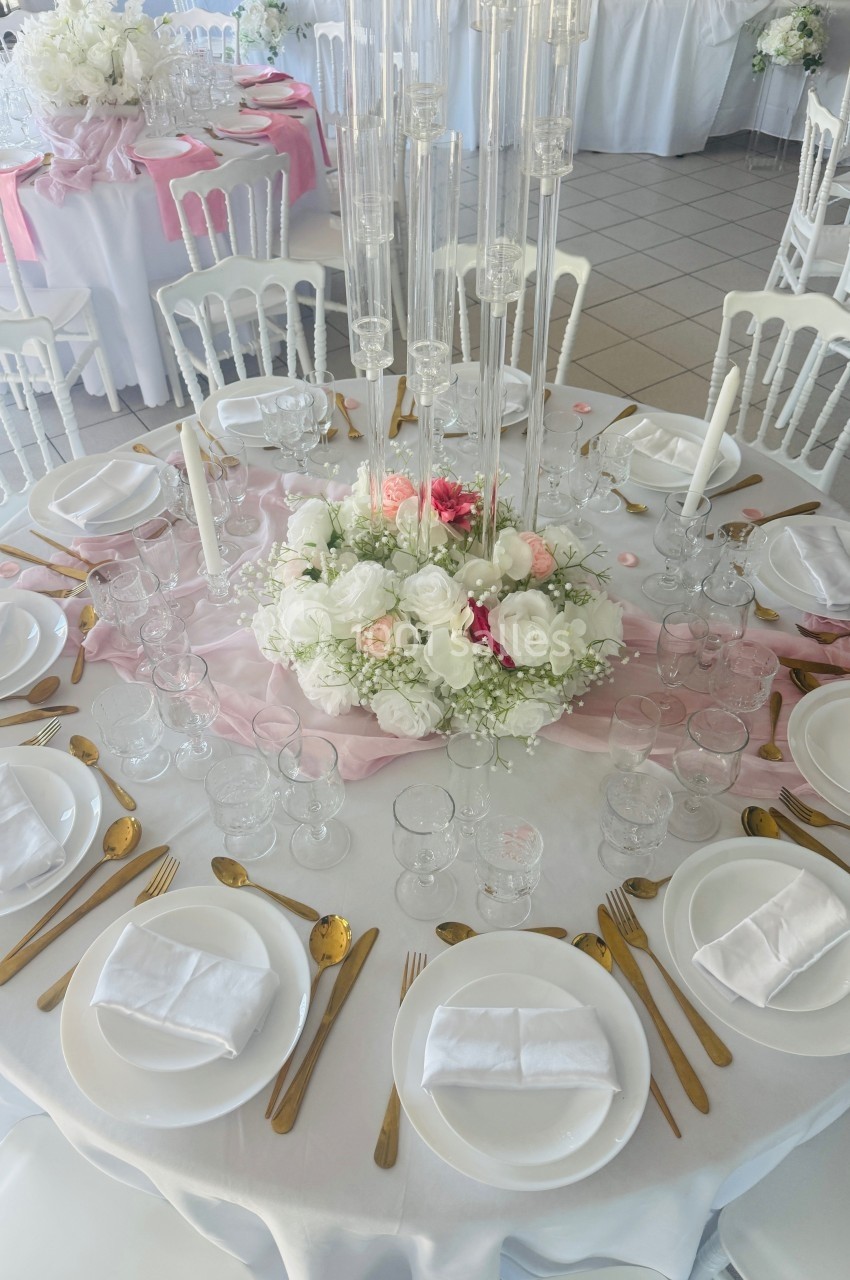 Table élégamment dressée avec vaisselle blanche, couverts dorés, centre de table floral et chandeliers en verre.