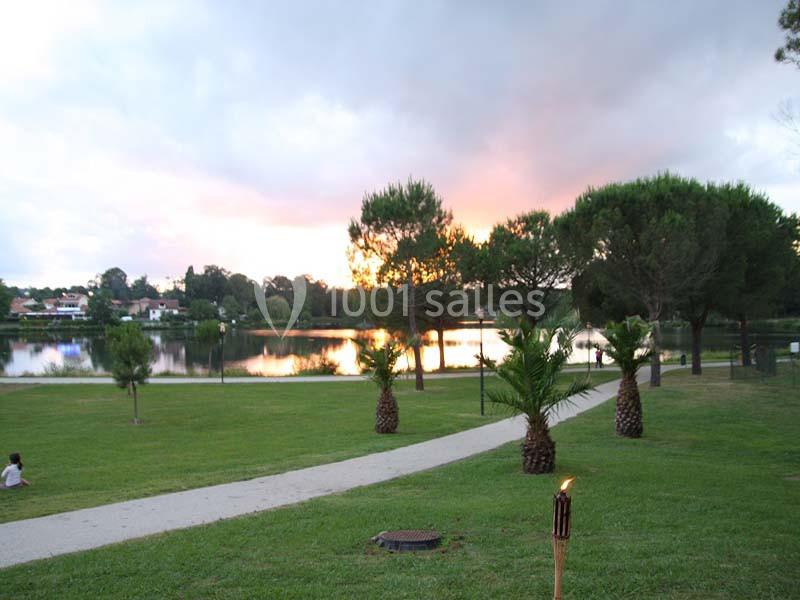 Vue d'un parc verdoyant avec des palmiers, un sentier, un lac et un ciel coloré au coucher du soleil.