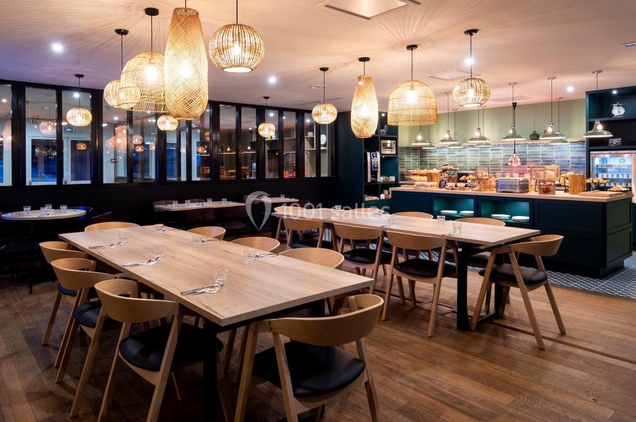 Salle de restaurant moderne avec tables en bois, chaises design et éclairage chaleureux par des suspensions en osier.