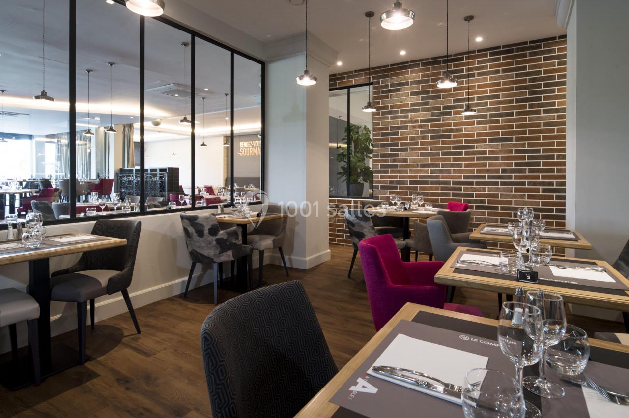 Salle de restaurant moderne avec tables dressées, chaises variées et murs en briques apparentes.