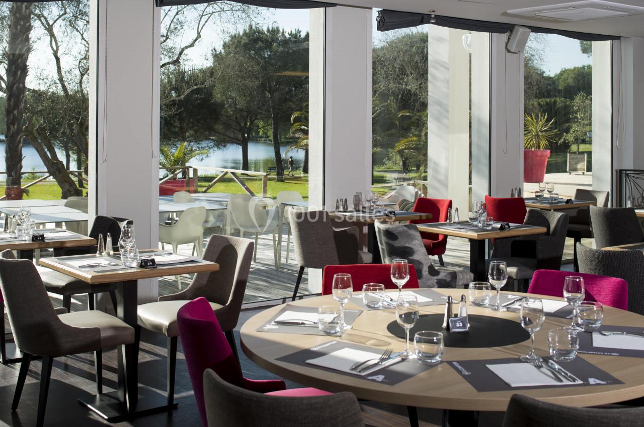 Salle de restaurant lumineuse avec grandes baies vitrées donnant sur un jardin et des tables dressées.