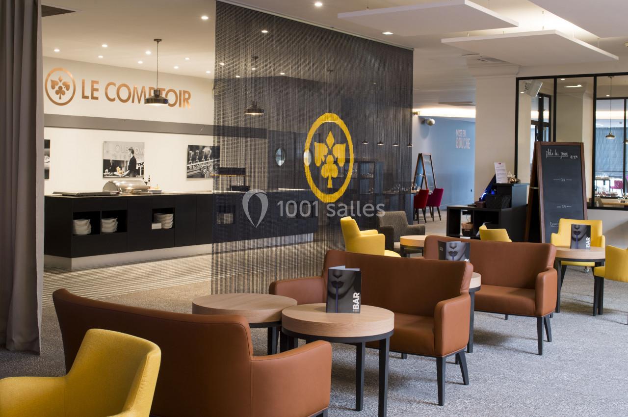 Espace lounge avec fauteuils et tables basses, séparé d'un comptoir de restauration par un rideau décoratif.