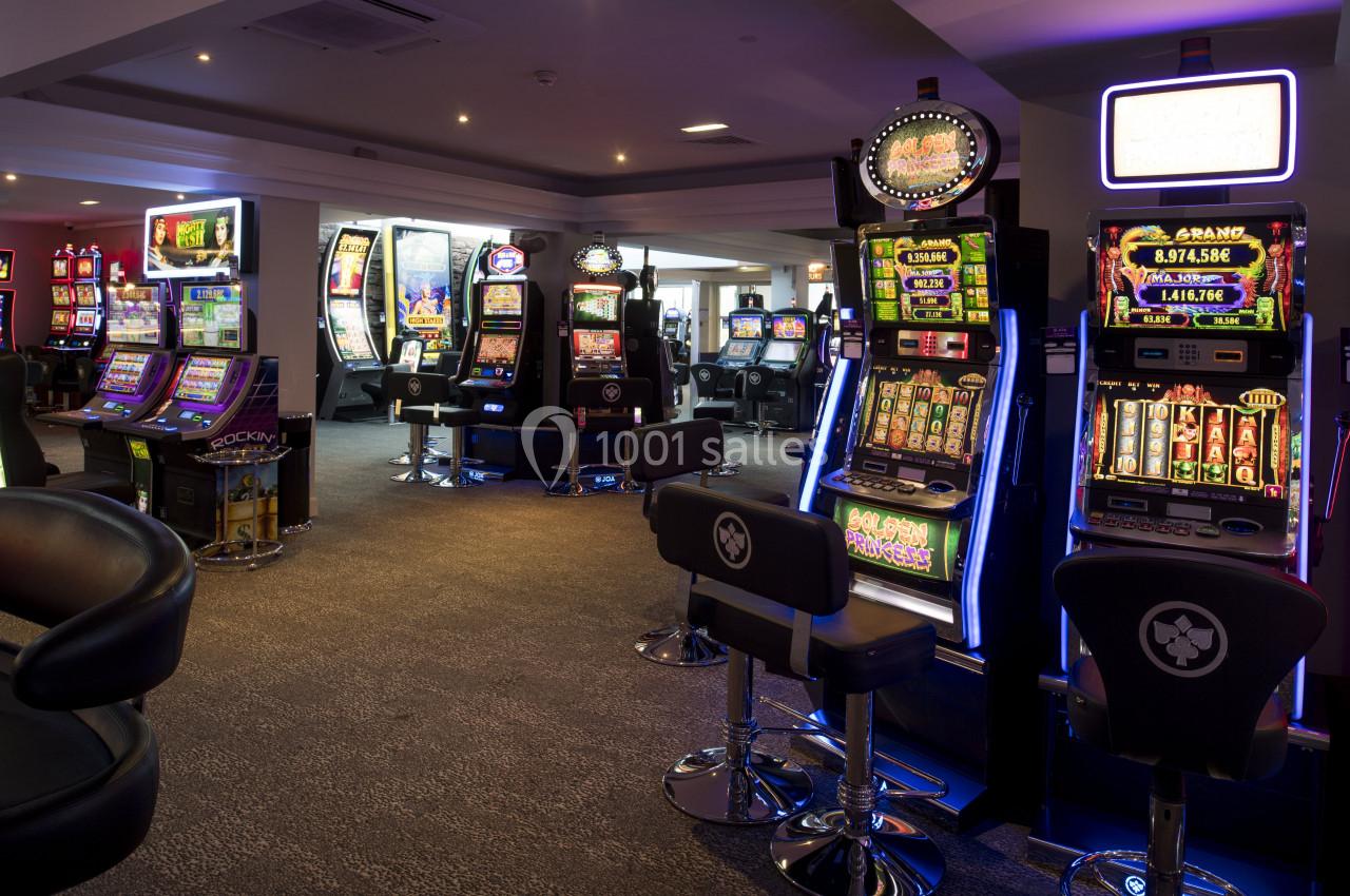 Salle de jeux avec plusieurs machines à sous illuminées et des sièges devant chaque appareil.
