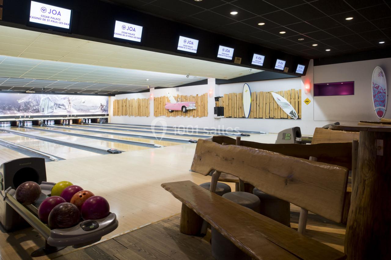 Salle de bowling avec plusieurs pistes, boules colorées au premier plan et décorations murales en bois et surf.