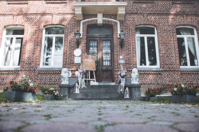 Salle de réception lumineuse avec tables dressées, lustres suspendus et nappes blanches sur des tables latérales.