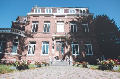 Salle de réception lumineuse avec tables dressées, lustres suspendus et nappes blanches sur des tables latérales.